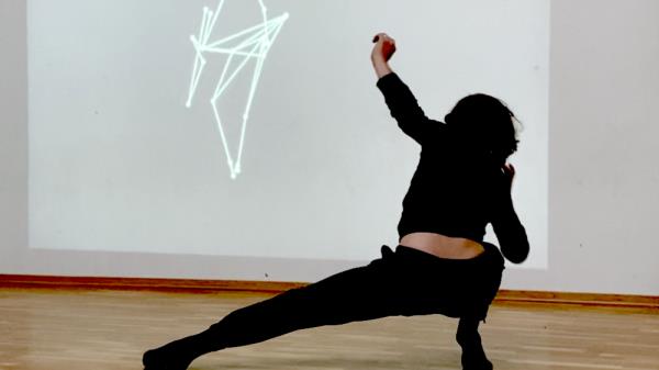 Dancer dancing in the foreground, with an AI image co<em></em>nsisting of lines, projected on a screen in the background