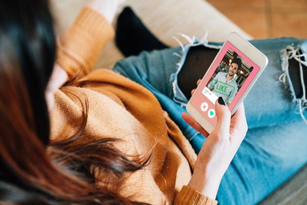 Young adult woman swiping on an o<em></em>nline dating app. She's using her smart phone on the sofa at home.